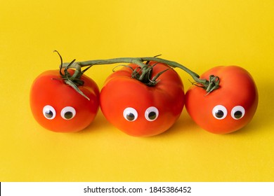 
Three red tomatoes connected by a green branch with toy big eyes on a yellow background