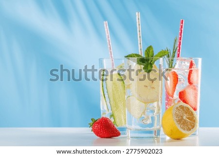 Three refreshing alcohol free drinks with strawberry, cucumber and lemon in glasses with ice on bright blue background. Healthy summer beverages concept