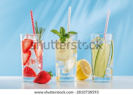 Three refreshing alcohol free drinks with strawberry, cucumber and lemon in glasses with ice on bright blue background. Healthy summer beverages concept