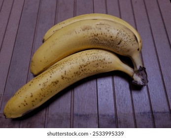 Three ripe bananas with brown spots on wooden floor - Powered by Shutterstock