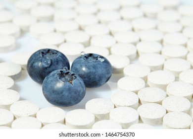 Three Ripe Blueberries Are Surrounded By Pills On All Sides. Concept: Natural Vitamins.