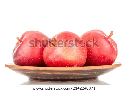 Three ripe red apples on a clay plate, macro, isolated on a white background.