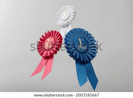 Three rosettes fly over gray background as prizes to winners and champions for quality and victory.