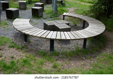 three round benches in the park. the grill is in the middle of sitting. large wood-paneled crescent moon in a meadow under a pergola. massive wooden blocks, terrace, plank, stripes, striped, board