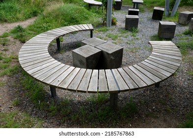 three round benches in the park. the grill is in the middle of sitting. large wood-paneled crescent moon in a meadow under a pergola. massive wooden blocks, terrace, plank, stripes, striped, board