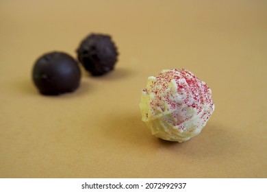 three round candies of white chocolate sprinkled with red sprinkles and dark chocolate lie on a beige background.  praline with truffles.  side view