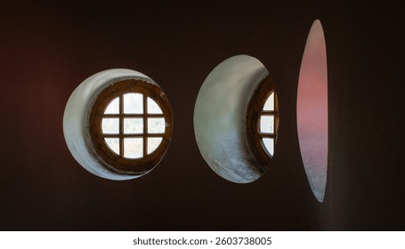 Three round windows on a plain pink wall, geometrical pattern