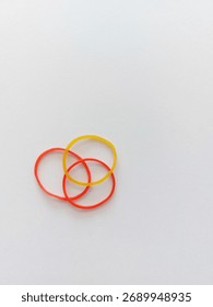 Three rubber bands (two red, one yellow) are intertwined on a white background.