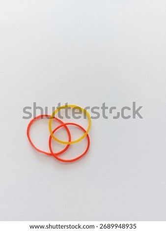 Three rubber bands (two red, one yellow) are intertwined on a white background.