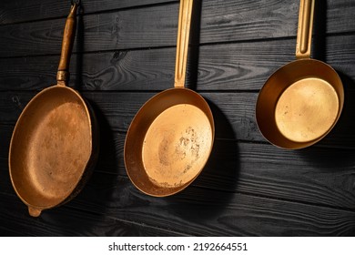 Three rustic copper fryingpans hanging on grey kitchen wall in restaurant or at home. Round empty gold or yellow pans with handles. Kitchenware, utensils for cooking and frying, interior decoration.