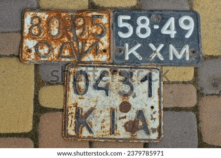 three rusty discarded identification marks taken from motorcycles, iron, dirty, with black numbers painted in white, numbers lying on a yellow concrete road during the day on the street
