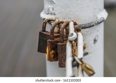 Three Rusty Padlocks Hanging On A White Pillar Near A Chain