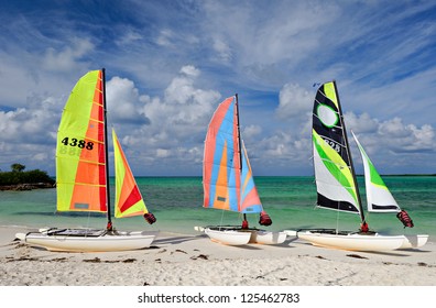 Three Sail Boats, Catamarans, On Tropical Beach With Blue Water Background