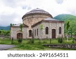 Three Saints Church, or the Round Temple, stands surrounded by lush greenery and misty mountains in Shaki, Azerbaijan