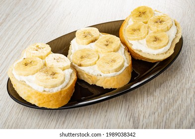 Three sandwiches with cottage cheese and banana in brown oval dish on wooden table - Shutterstock ID 1989038342