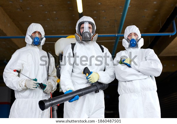three sanitation workers in protective gear\
suit, medical mask, gloves and goggles with pressure washer or\
sanitizer over city street\
background