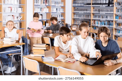 Three schoolchildren preparing for lessons in the school library are looking for the necessary information on a laptop, ..discussing topical issues