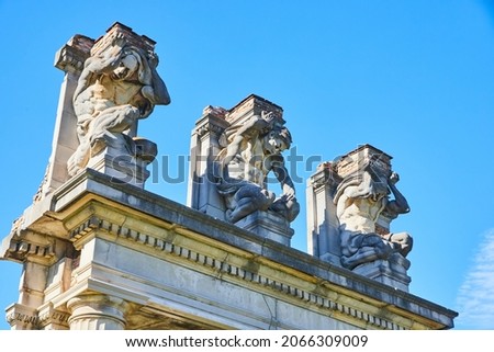 Three sculptures of men at top of old ruins against blue sky