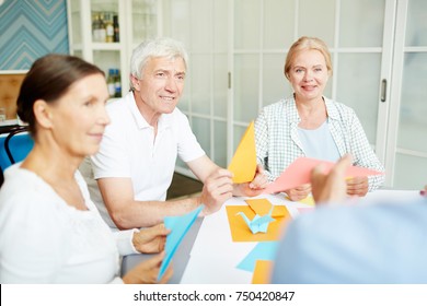 Three Senior Friends Listening To Coach During Master-class On Making Origami From Colorful Paper