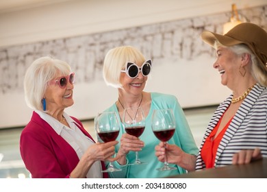 Three senior happy ladies having a party and looking enjoyed while drinking wine