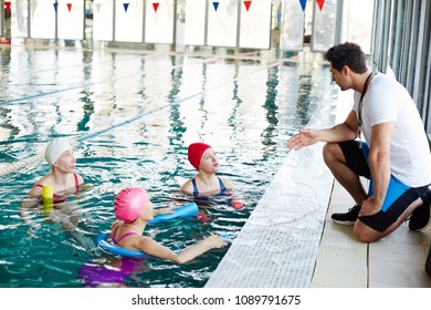 Three senior swimmers in water talking to their young trainer recommendations before swimming - Powered by Shutterstock