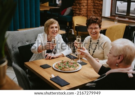 Three senior women friends having dinner at restaurant with pizza and wine, attractive lady spending time together indoors. old friends celebration meeting in modern cafe. 