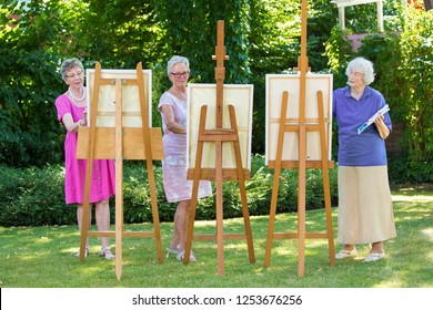 Three senior women painting on canvas in garden during sunny day. - Powered by Shutterstock