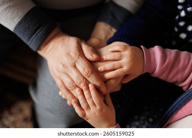 Three sets of hands interlock in a warm gesture of affection and connection, highlighting the bond between family members during a cozy indoor gathering at home.