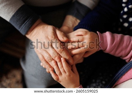 Three sets of hands interlock in a warm gesture of affection and connection, highlighting the bond between family members during a cozy indoor gathering at home.