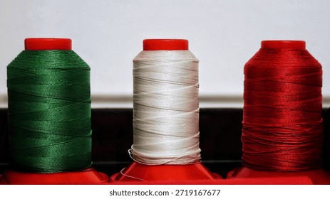 Three sewing thread spools in green, white, and red forming the Italian tricolor. Concept of craftsmanship, Made in Italy, tailoring, fashion industry, national identity, and textile manufacturing.