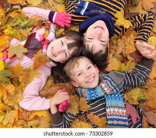 	Three siblings laying in autumn leaves.