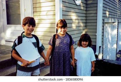 Three Siblings On Their First Day Of School, Posing In Front Of The House.  Vintage Scan Of 1990s Family Photo (1997).