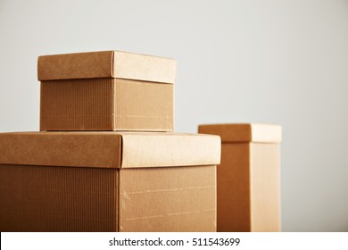 Three similar beige corrugated cardboard boxes with covers of different shapes and sizes isolated on white