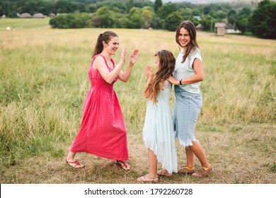 Three Sister Girls Playing On The Park Outdoor. 3 Girls, Sisters, Girlfriends In The Field. Happy Mother With Younger And Older Daughter, Two Children Plays In The Meadow In Summer In Dresses.