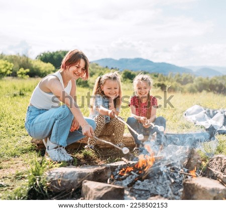 Three sisters cheerfully smiling while they roasting a marshmallows candies on the sticks over the campfire flame. Happy family or outdoor picnic activities concept image.	