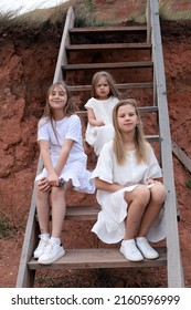 Three Sisters In White Dresses Are Sitting On The Stairs.