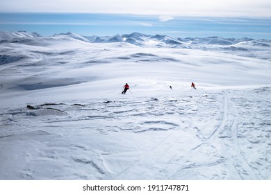 Three skiers skiing towards the mountain ranges in the horizon down untracked powder snow field while heliskiing in Lapland Sweden