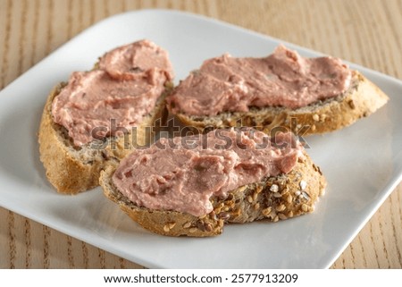 Three slices of bread spread with a pink, smooth, and spreadable pâté made with red onion and butter, on a white plate.