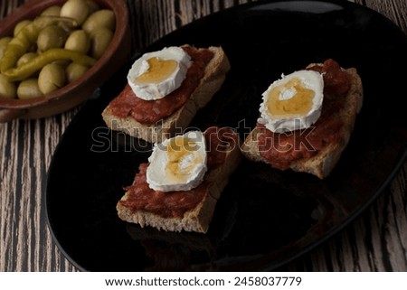 Three slices of toasted bread with sobrasada, goat's cheese and honey, accompanied by the corresponding pickles.