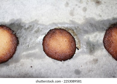 Three Slightly burnt, misshapen, homemade sugar cookies lined up on greasy, dirty-looking parchment paper.  Two of the cookies are bisected by the shot. - Shutterstock ID 2253089581