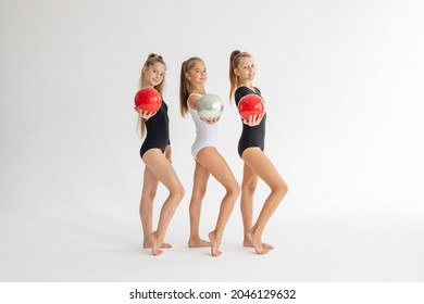 three slim artistic teenager girls in black and white leotards trains and having fun with balls on white background in rhythmic gymnastic exercise, children's professional sports