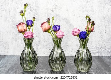 Three Small Green Flower Bud Vases Filled Each With Pink And Purple Lisianthus Flower. Gray Background, Black Table. Space For Text.