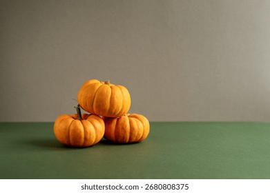 Three small orange pumpkins stacked on a green surface. The background is a neutral gray, creating a seasonal autumn atmosphere with copy space.