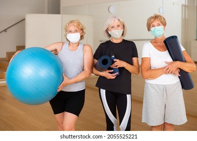 Three Smiling Aged Women In Sportswear And Protective Masks Standing In Fitness Studio With Sports Equipment In Hands, Ready For Training. Healthy Lifestyle And Pandemic Precautions Concept