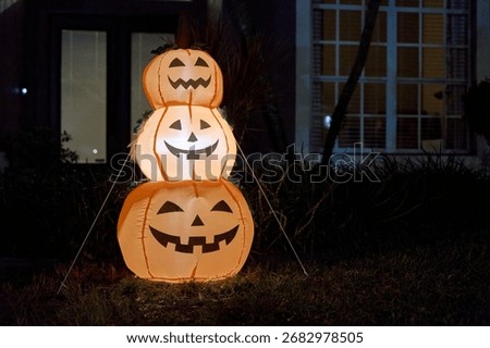 Three smiling jack-o-lantern inflatables are tied and glowing outside a house after dark. Warm light and orange color create a cheerful, festive Halloween yard display.