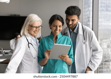 Three smiling physicians using tablet, engaged in collaborative discussion and successful teamwork, working on-line, learn new modern telemedicine application, focusing on content displayed on device - Powered by Shutterstock