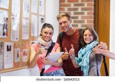 Three Smiling Students Standing Next To Notice Board Showing Thumbs Up In School