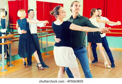 Three smiling young couples dancing tango in the hall. Selective focus