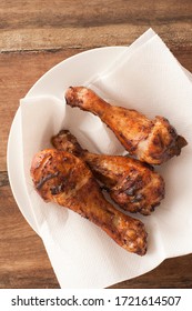 Three Spicy Grilled Chicken Legs Served On A Paper Napkin On A Plate For A Tasty Finger Snack , Overhead View On A Wooden Table