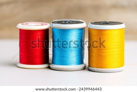 Three spools of thread in vibrant red, blue, and yellow stand in a row against a neutral background, illustrating the basic tools of sewing and textile arts.